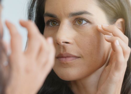 Woman with aging skin looking at her face in the mirror