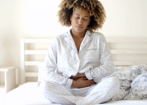 Woman suffering from endometriosis sitting in bed, clutching her stomach