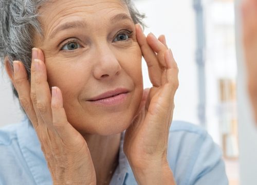 Older woman with skin laxity looking at her face in the mirror